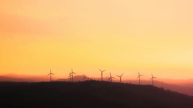 Silhouette of wind turbines at sunset, promoting sustainable energy.