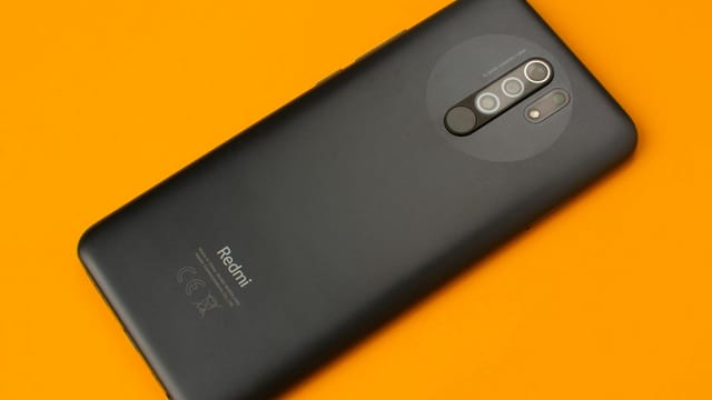 Black smartphone placed on a vivid orange background, showcasing sleek design and multiple cameras.