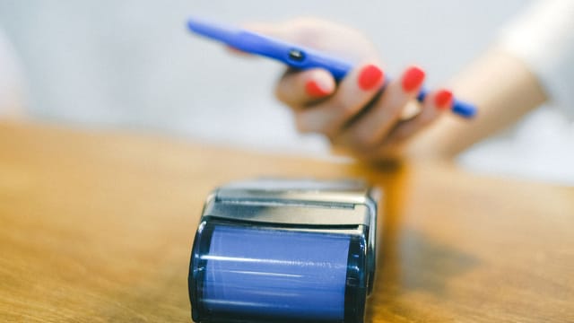 Close-up of hand using smartphone for contactless payment at a terminal on wooden surface.