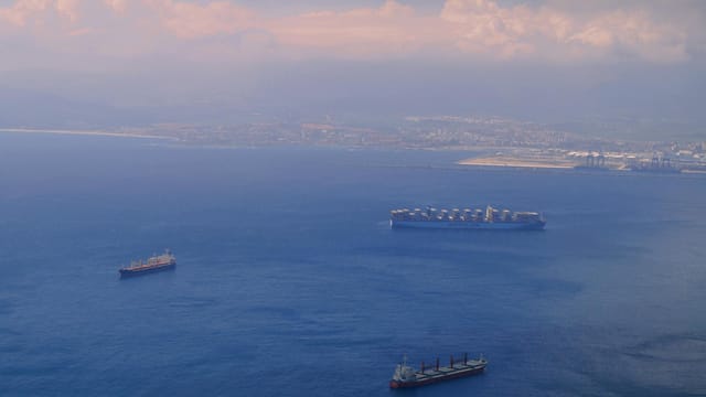 Aerial view of cargo ships navigating through the picturesque waters near Gibraltar's coastline.