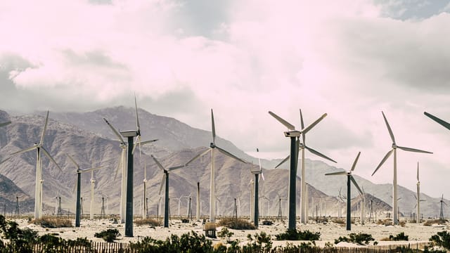 Capture of a wind farm set against a dramatic mountain backdrop under a cloudy sky.