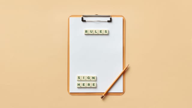 Flat lay of clipboard with letter tiles spelling 'rules' and 'sign here', accompanied by pencil on beige background.