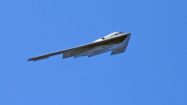 A B-2 Spirit stealth bomber flying in clear blue skies, showcasing its advanced aerodynamics.