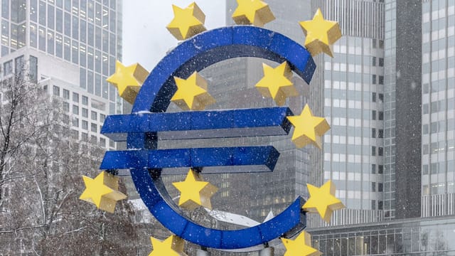 The iconic Euro symbol stands prominently amidst snowy Frankfurt skyscrapers.
