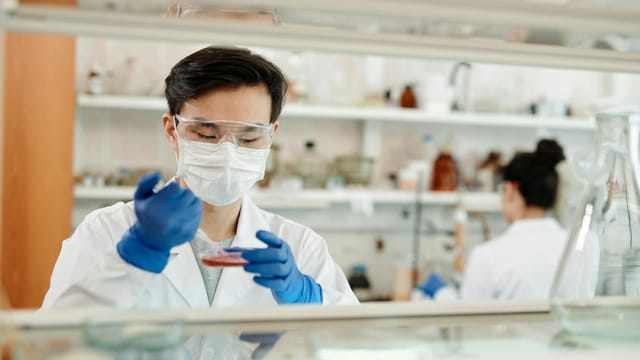 Researcher in a lab coat working on a scientific experiment with a petri dish and protective gear.