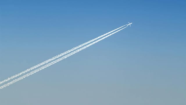 An airplane creating contrails across a clear blue sky, showcasing aviation technology.