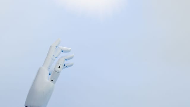 A robotic hand reaching towards a bright light on a white background symbolizing innovation.