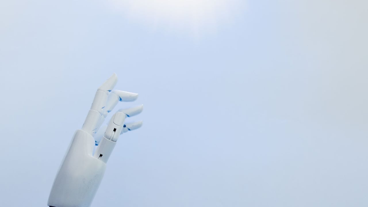A robotic hand reaching towards a bright light on a white background symbolizing innovation.