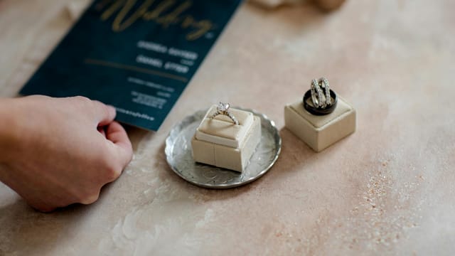 Close-up of wedding invitation and diamond rings on a tray, showcasing elegance and preparation.