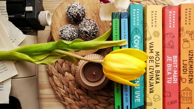 Top view stack of books on table near beautiful yellow tulip and orchid flowers arranged with chocolate truffles placed on wicker placemat