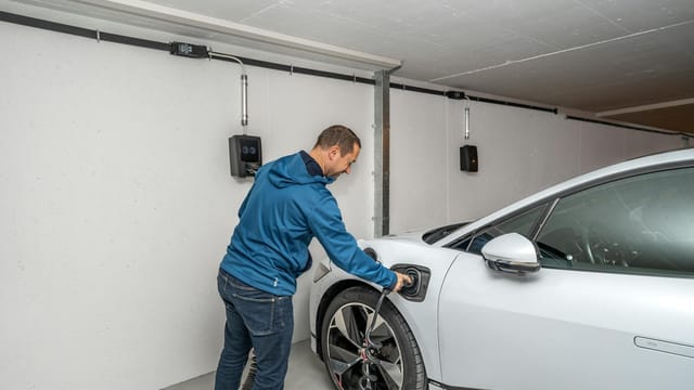 A man connects an electric car to a charging station in a modern indoor garage setting.