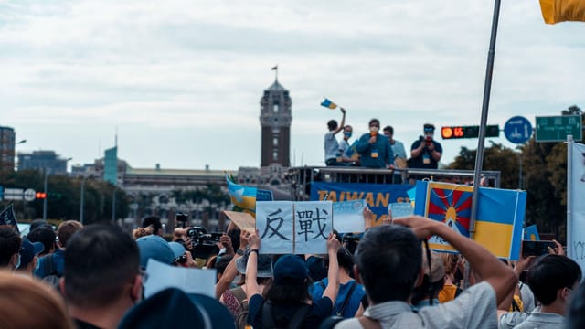 Crowd protests with various flags and signs in front of prominent building.