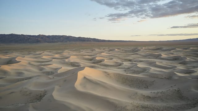 Picturesque view of dry sand hills with loose texture located near ridge under blue sky with clouds in evening time