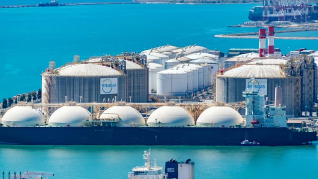 Aerial shot of a gas terminal featuring LNG storage tanks and tanker ships in turquoise waters.