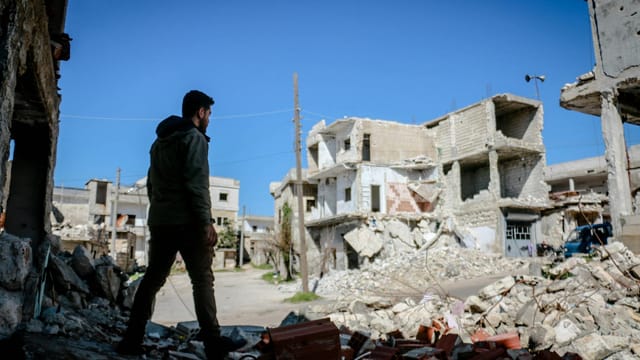 A man walks through the rubble of destroyed buildings in Idlib, Syria, highlighting urban devastation.