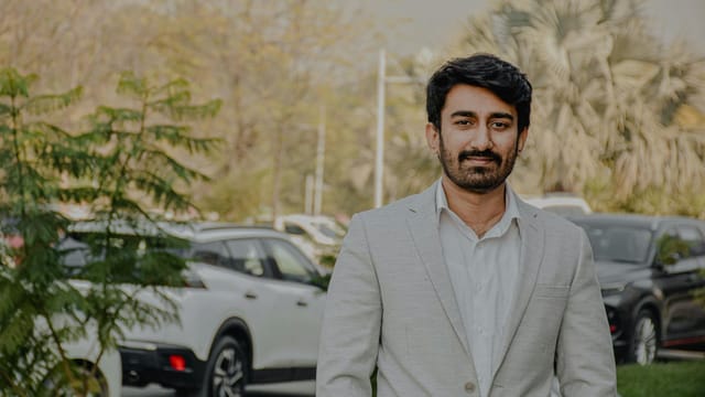 A man in a light suit standing outdoors in Islamabad, Pakistan, exuding confidence.
