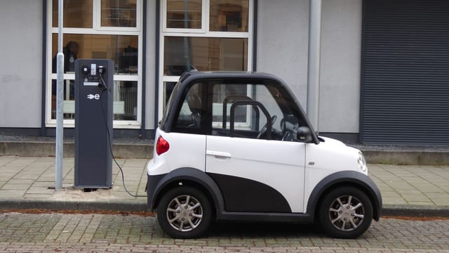 A white and black compact electric car charging at a public power station.