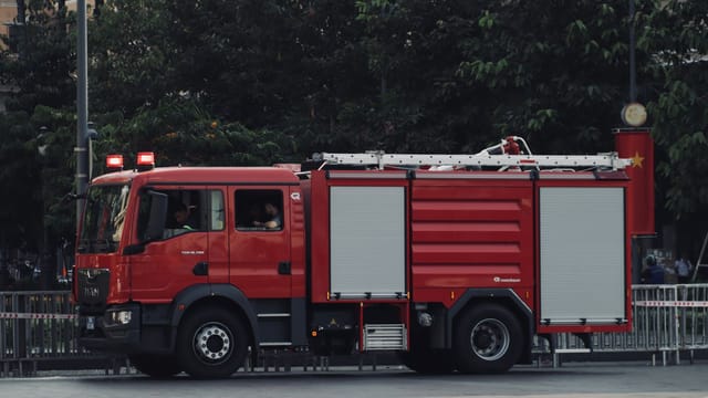 A vibrant red fire truck is parked on a city street surrounded by trees, showcasing urban emergency readiness.