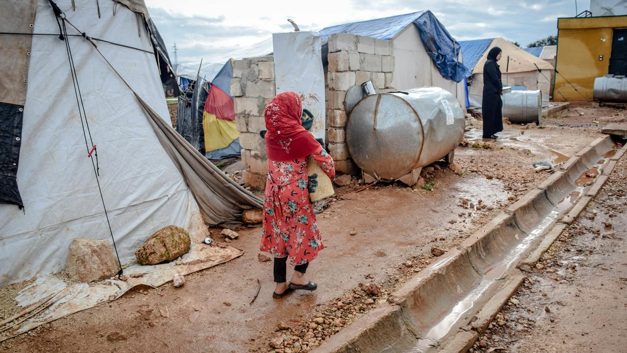 Full body of poor women in hijabs and headscarves near weathered buildings and camps in village under cloudy sky