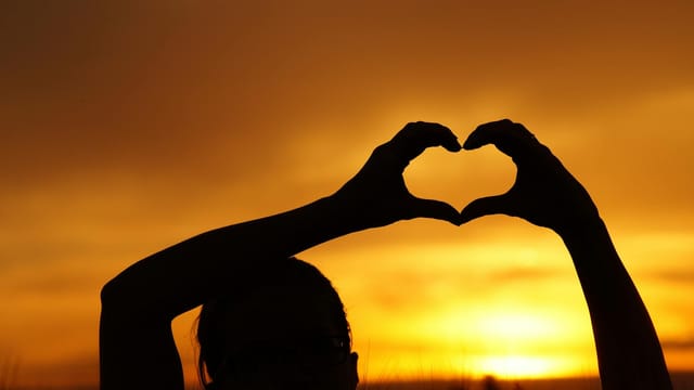A silhouette of a person forming a heart shape with hands against a stunning sunset.