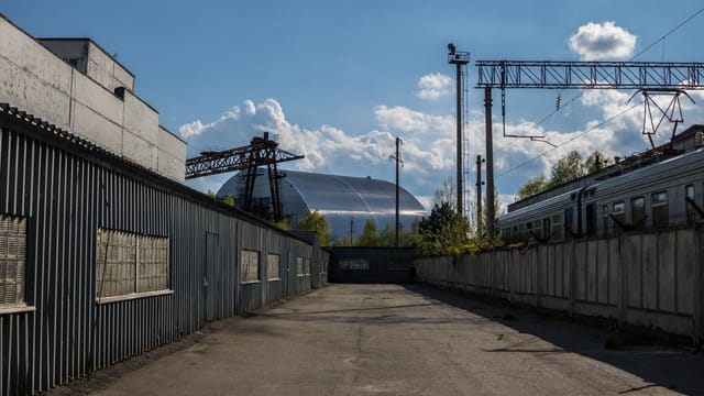 View of Chernobyl's new safe confinement and railway tracks under a blue sky.