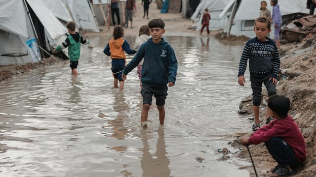 Children navigate a flooded area in a Gaza refugee camp, highlighting resilience.