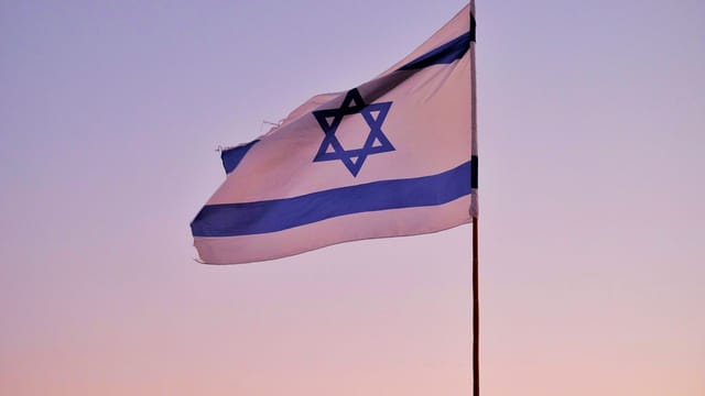 Israeli flag on a flagpole against a serene sunset sky, symbolizing national pride.