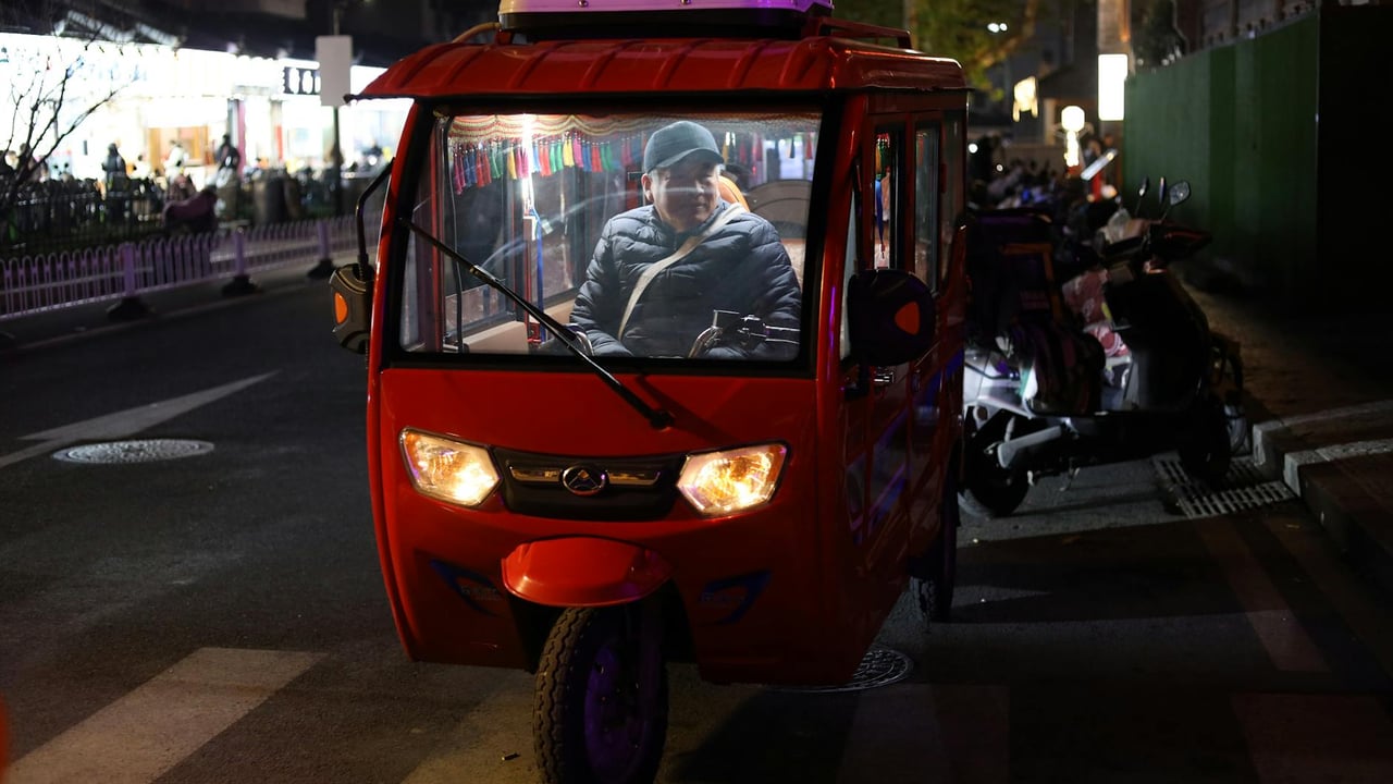 A red tuk-tuk on a busy street at night in Nanjing, China, with a driver inside.