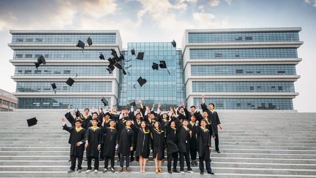 Group of graduates celebrating and tossing caps outside modern building.
