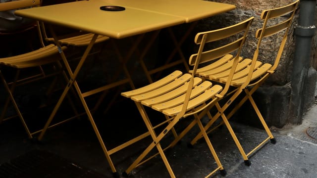 Foldable yellow bistro chairs and table on a Turin street, offering a cozy, urban ambiance.