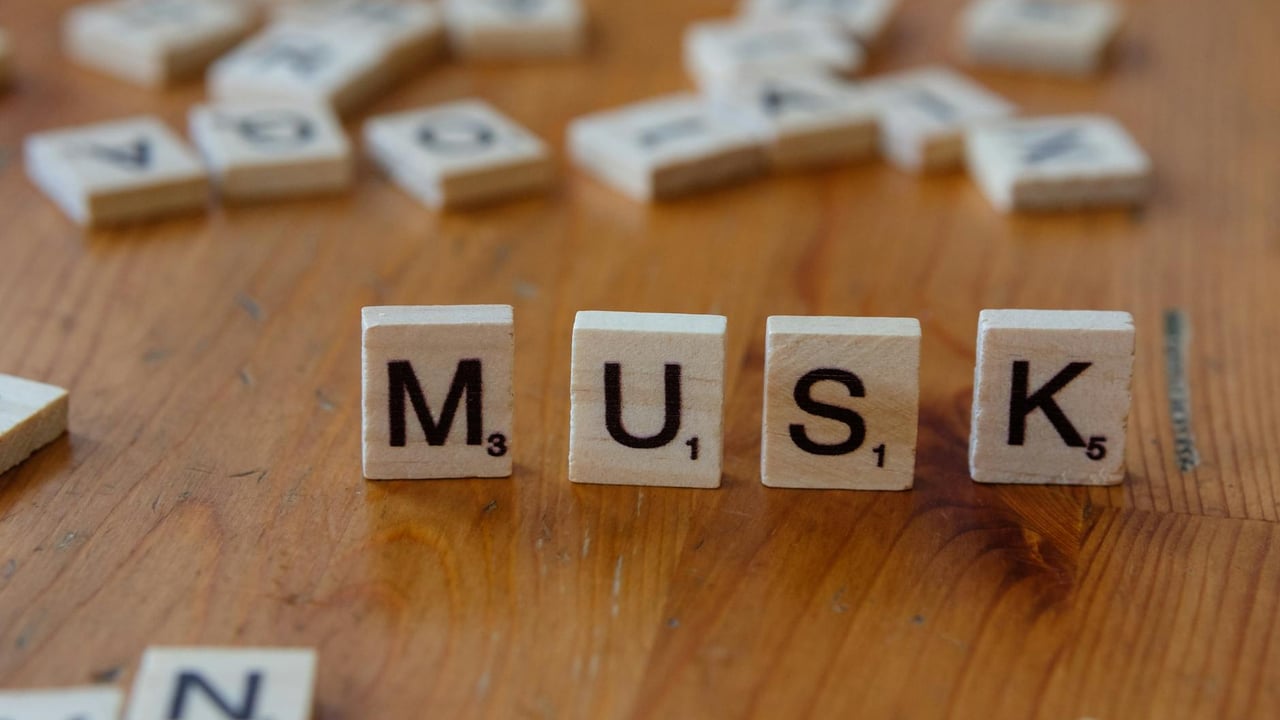 Close-up of Scrabble tiles spelling 'MUSK' on a wooden table, ideal for business and innovation themes.