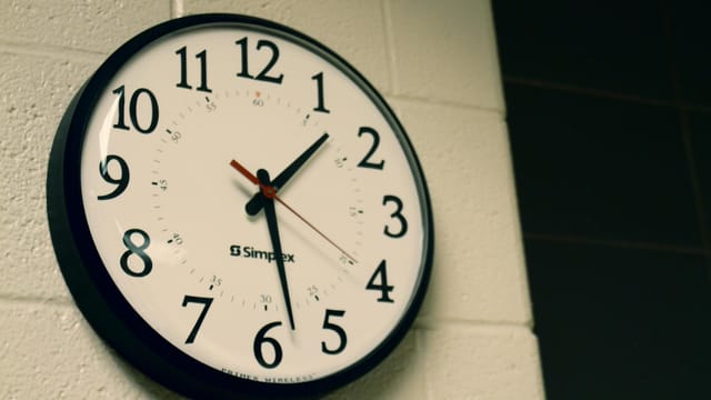 Simplex wall clock on a white brick wall, depicting time and simplicity.