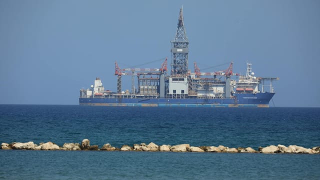 An offshore drilling rig floats on a calm sea with a clear blue sky in the background.