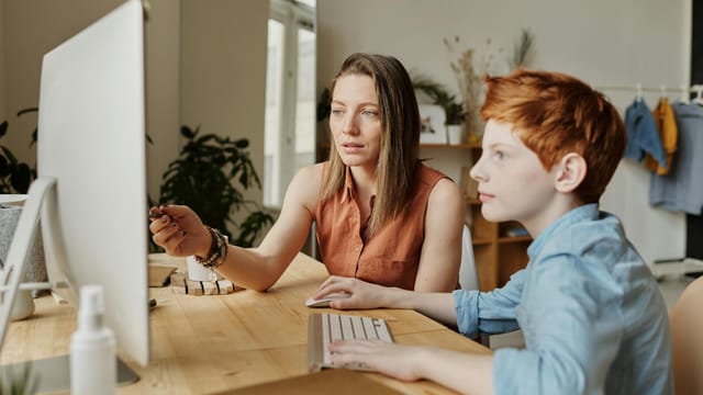 A mother and her son attentively engaged in online learning at home on a computer.