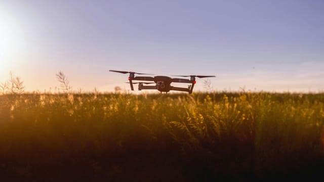 A drone flies over a field during sunset, capturing stunning aerial views.