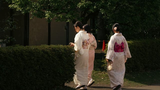 Three women in traditional kimonos strolling in a serene Tokyo garden, capturing cultural elegance.