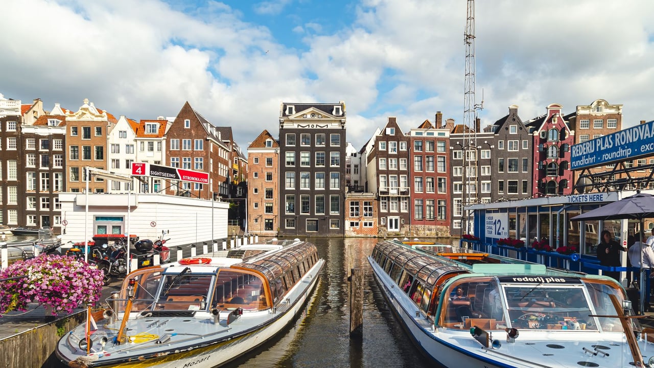 Scenic view of Amsterdam's iconic canal houses and tour boats on a sunny day.