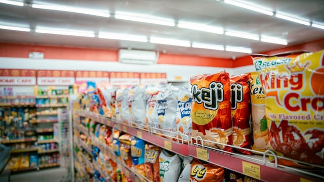 Wide shot of vibrant snack aisle in a supermarket with various chip bags on display.