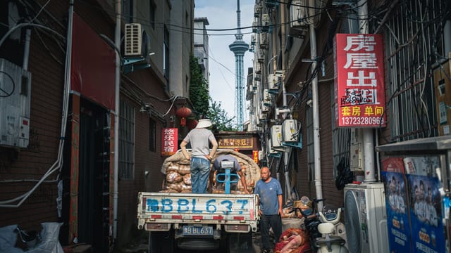 Street scene with workers unloading a truck in a narrow urban alley.