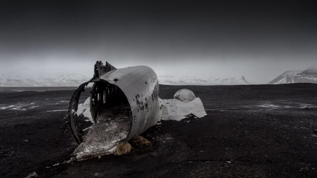Eerie scene of a plane wreck on a desolate black sand beach under a gloomy sky.