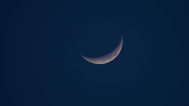 A close-up of a crescent moon against a dark night sky, highlighting lunar details.