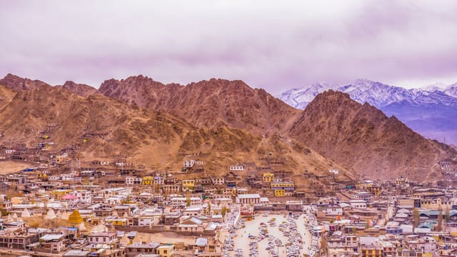 Colorful town surrounded by majestic mountains under overcast sky, showcasing breathtaking natural beauty.