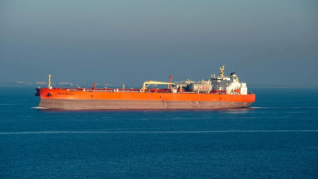 Bright orange LNG carrier ship cruising through calm sea waters on a clear day.