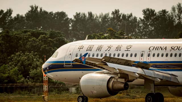 China Southern Airlines plane on runway, surrounded by lush greenery.