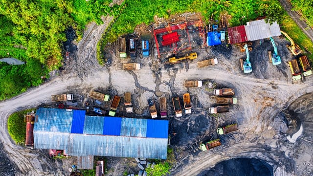 Aerial photograph of an industrial mining site in Rumpin, Indonesia, featuring trucks and excavators.