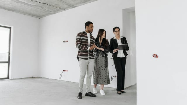 Real estate agent with clients exploring an unfinished apartment interior.