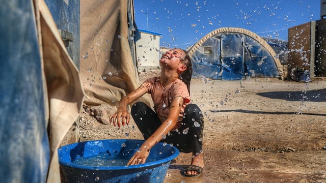 A child enjoying water play in a Syrian refugee camp under sunlight.