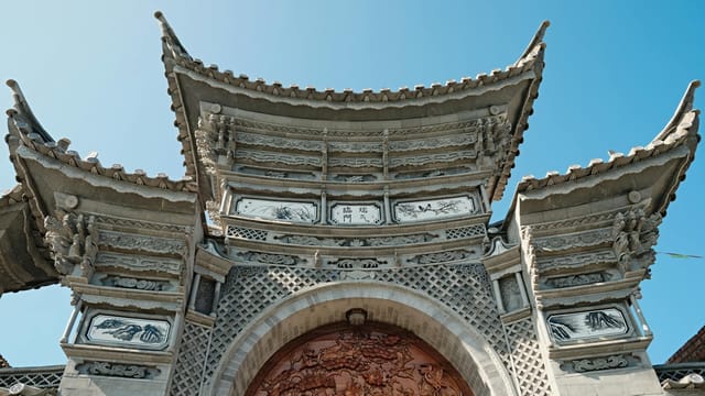 Intricately carved traditional Asian gate with detailed stone and woodwork under a clear blue sky.