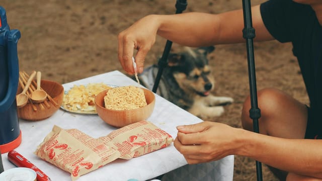 Close-up of cooking instant noodles outdoors with a dog nearby.