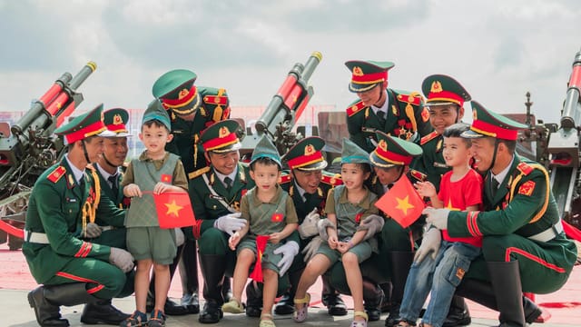 Vietnamese soldiers interact with children holding flags during a daytime event outdoors, showcasing national pride.